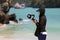 The video photographer or journalist wearing a mask and recording the tourist activities on the beach during the spread of the