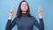 Video portrait of a charming serious girl student with glasses raising her hands up on a blue background