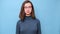 Video portrait of a charming serious student girl with glasses in a blue sweater looking at you and blinking