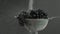 In the video we see grapes in a sieve, water starts fall from the top in a jet, camera goes from left to the right, grey