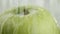 In the video we see a green apple, the water begins to pour from the top like a shower, white background, close-up