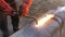 Video view of the welder through the fire. A welder in protective clothing in the open air cuts metal pipes with