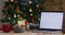 Video of wooden table with christmas decorations and laptop with blank screen over christmas tree