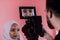 Videographer in digital studio recording video on professional camera by shooting female Muslim woman wearing hijab