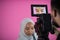 Videographer in pink studio recording video on professional camera by shooting female muslim woman