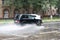 Vidnoe, Russia - August 12, 2020: Russian car Niva raising a sick wave of rainwater, auto driving in the rain, heavy downpour.