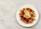 Viennese waffle with banana slice and honey on a white round plate on a light gray background