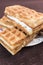 Viennese waffles with vanilla-cream filling are on a saucer on a dark brown background