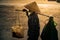 Vietnamese with conical hat carries a yoke on her shoulder along the street.