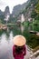 Vietnamese Girl with straw hat in Trang An Scenic Landscape formed by karst towers and plants along the river (UNESCO World