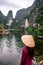 Vietnamese Girl with straw hat in Trang An Scenic Landscape formed by karst towers and plants along the river (UNESCO World