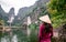 Vietnamese Girl with straw hat in Trang An Scenic Landscape formed by karst towers and plants along the river (UNESCO World