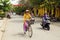 Vietnamese people on a bicycle and motorbikes on a road in the center of city with yellow houses and red and yellow decorations