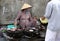 Vietnamese woman on the street market selling snacks, heated on a special oven on coals