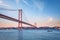 View of 25 de Abril Bridge over Tagus river, Christ the King monument and a yacht boat at sunset. Lisbon, Portugal