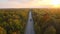 View from above of backcountry road between colorful woods at sunset. Narrow highway surrounded with yellow and orange