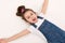 View from above of Caucasian mischievous baby girl in blue denim overalls, lying down on a white background. Copy space