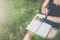 View from above. Close-up of notepad lying on girl`s lap.Girl sitting in garden on lawn under tree uses smartwatch