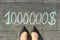 View from above, female feet with text 1000000 dollar written on grey sidewalk.