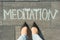View from above, female feet with text meditation written on grey sidewalk.