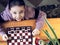 View from above. The girl learns to play table chess and cheerfully looks up at the camera. Board games are an alternative to