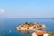 View from above of island and St. Stefan's beach in Budva. Blue sky and sea with boats and sailboats, sunny day