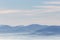 A view from above of a valley filled by a sea of fog, with various layers of emerging hills and mountains with different shades o