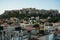 View of the Acropolis, Erechtheion, from Monasteraki Square through old town neighborhood buildings and Hadrian`s Library ruins