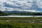 View across a lake in Sweden with bright sky, green forest and some wind power plants in the distance on top of a mountain