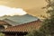 A view across the rooftops towards the silhouette of a smoking Mount Etna