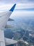 View through airplane porthole with cultivated fields, blue sky, light clouds and part of airplane wing