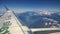 View from airplane window of mountains with snow on the top, clouds, wing and blue sky