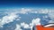 View from the airplane window to the blue sky and white clouds, an orange turbine on the wing of the plane, a view of