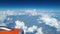 View from the airplane window to the blue sky and white clouds, an orange turbine on the wing of the plane, a view of