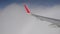 View of airplane wing above clouds through plane window