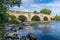 A view along the rocky shore towards an old medieval bridge over the River Ure on the outskirts of Ripon, Yorkshire, UK