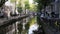 View of Amsterdam city: early morning, cloudy day, Autumn - cars and bicycles parked along the canal, trees reflected in