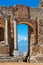 View through the ancient archway of the Theatro Greco on the smoking volcano Mount Etna, Sicily, Italy