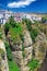 View on ancient village Ronda located precariously close to the edge of steep cliff, clear blue sky with fluffy cloud - Andalusia