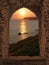 View through arched castle window to sunset coastal landscape, c