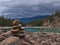 View of Athabasca River surrounded by forest and rocks with pile of stones in front and snow-capped Rocky Mountains, Canada.