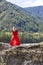 View from the back of Blonde woman in red dress fluttering in the wind stands on the rock stones on banks of Katun river against