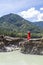 View from the back of Blonde woman in red dress stands on the rock stones on banks of Katun river against background of mountains