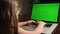 View from the back girl sitting at table and typing on laptop green chroma key