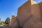 View from back and side of the San Francisco de Asis Mission Church in Taos New Mexico showing one bell tower with cross and birds