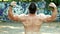 View from the back of silhouette of athletic man with a bare torso posing shows his muscles and biceps against the