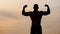 View from the back of silhouette of athletic man with a bare torso posing shows his muscles and biceps against the sky
