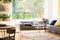 View of the backyard through a large window in a natural living room interior with plants, wooden furniture and a comfy sofa