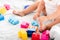 View of barefoot baby in white clothes sitting on bed and playing with bright construction