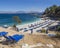 View of Bataria white sand beach with blue sunbeds and tourist people at Kassiopi Bay, and Albanian mountains from the